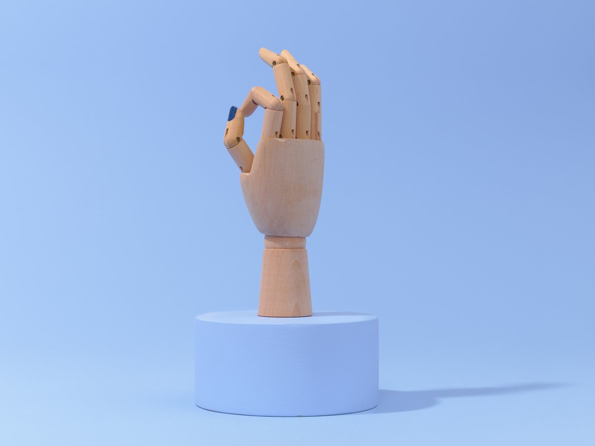 Een mannequinhand met gelakte nagels, geplaatst op een verhoogd rond platform. De achtergrond is zachtblauw en creëert een rustige sfeer.