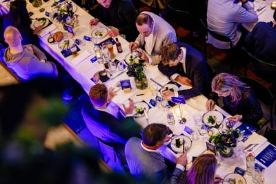 Luchtfoto van een formeel diner met gasten aan een lange tafel, gedekt met elegant serviesgoed, bloemstukken en menu's