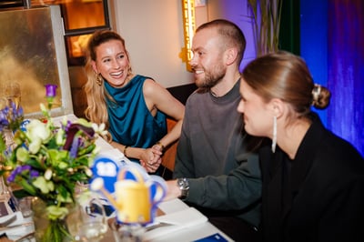 Een groep van drie mensen zit aan een eettafel en voert een levendig gesprek. 