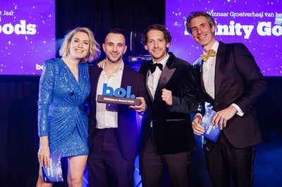 Vier mensen glimlachen op het podium tijdens een prijsuitreiking. Eén van hen houdt een plaquette met de tekst ‘bol.