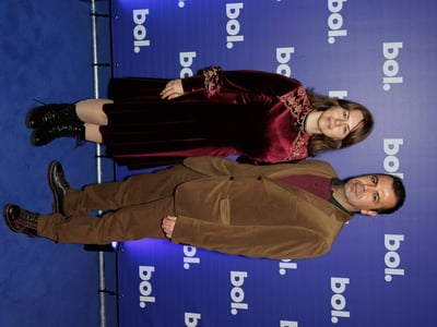 Een man en een vrouw poseren op een blauw tapijt voor een achtergrond met ‘bol.’-logo's.