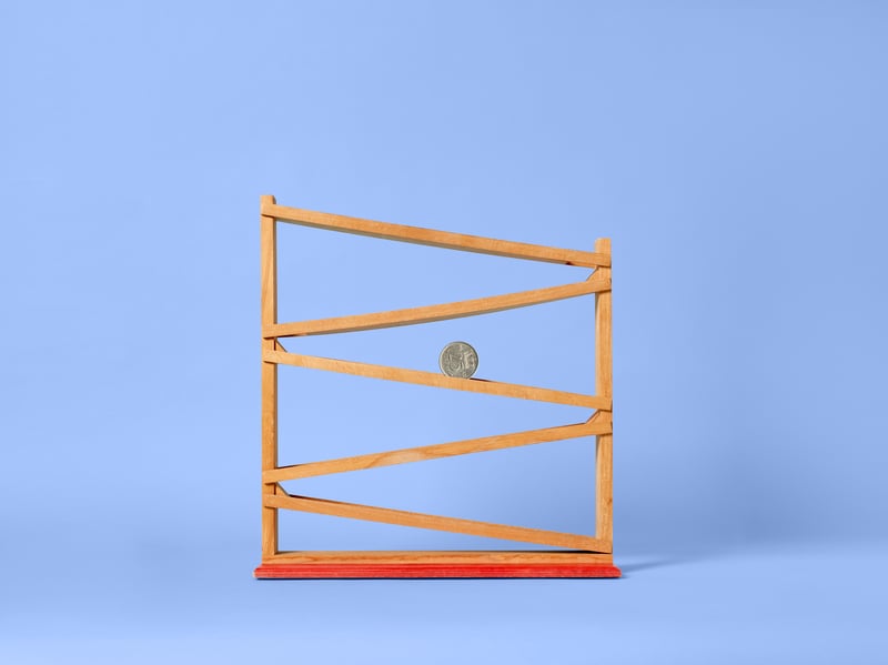 A wooden marble run on a blue background, with zigzag tracks and an orange base. A single marble rolls down.