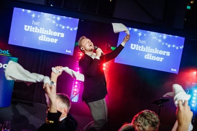 Een man zingt vol passie met een microfoon tijdens een evenement met de titel ‘het Uitblinkers diner’