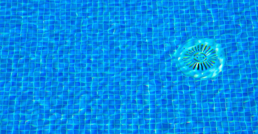Detail of mosaic tile floor and drain cover in a swimming pool seen through rippled water.