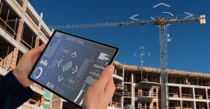 Builder with a digital tablet controls a remote-controlled unmanned crane. Digital transformation in construction industry.