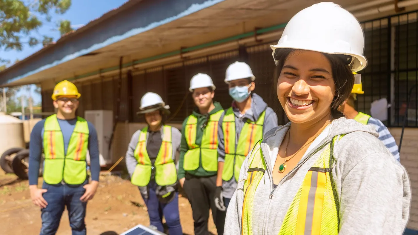 Young woman in high-vis vest smiling on a construction site with other team members Young woman in high-vis vest smiling on a construction site with other team members