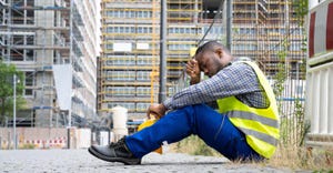 Unhappy construction worker in yellow vest sitting outside jobsite on the sidewalk