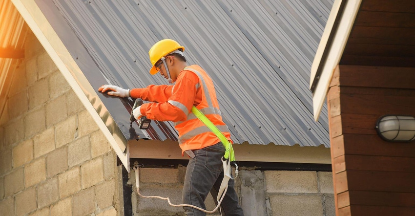 Roofer wearing high-vis orange vest and hard hard attaching metal sheets to roof in Thailand