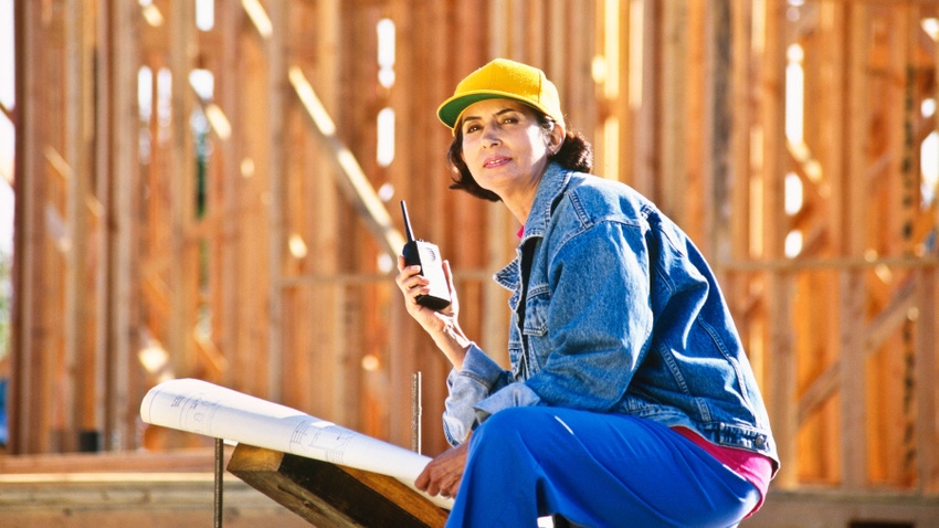 Hispanic Woman heads up construction site using her walkie talkie and blueprints