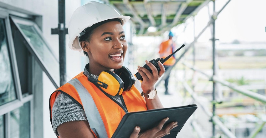 Construction worker with tablet, walkie talkie or radio talking, instructing and checking building progress on development