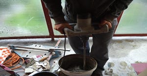 An unidentifiable contractor mixes stucco in a white plastic drum in preparation of applying it to a home remodel project.