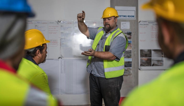 Construction contractor in high-vis vest and hat leads team meeting