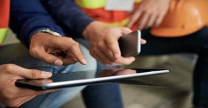 Construction workers looking at an iPad or tablet with one holding a cellphone 