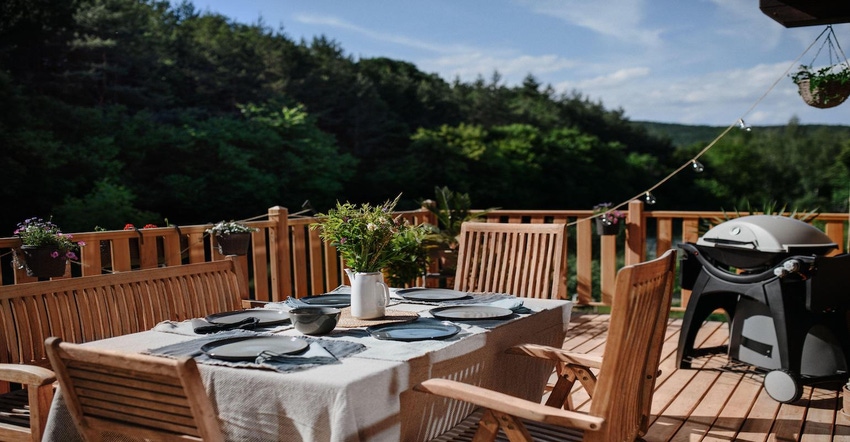 Dining table with wooden chairs set for dinner on the terrace with grill 