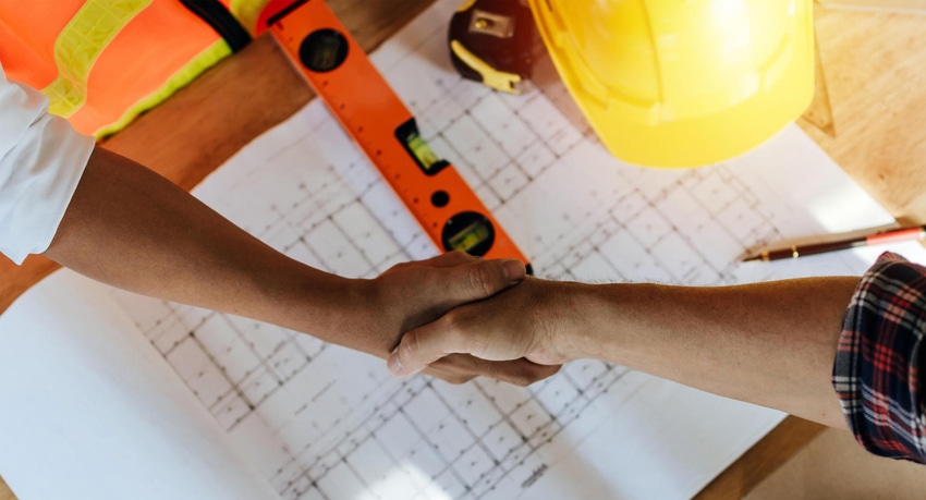 Roofing contractor and client handshake over building plans and tools