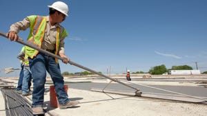 Texas highway construction worker smooths out freshly poured concrete with large trowel on stretch of road in Austin