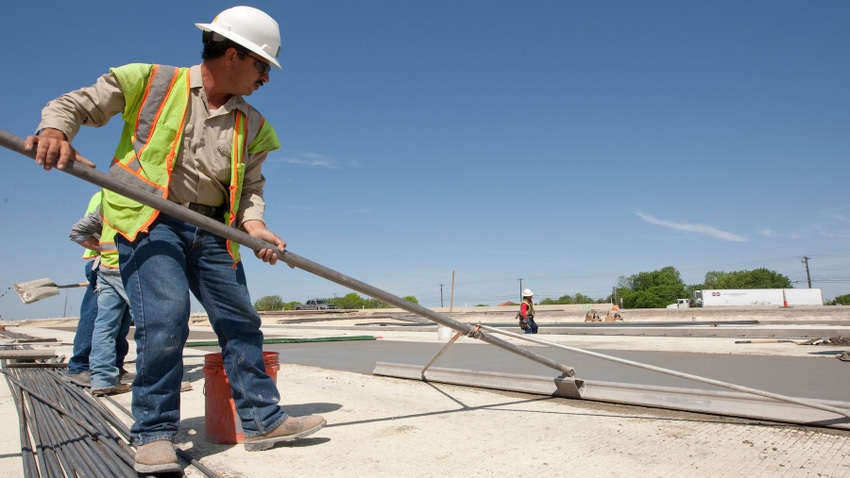 Texas highway construction worker smooths out freshly poured concrete with large trowel on stretch of road in Austin