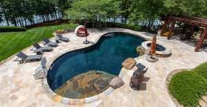 Luxurious outdoor pool with landscaping, in the backyard of a home, overlooking lake.