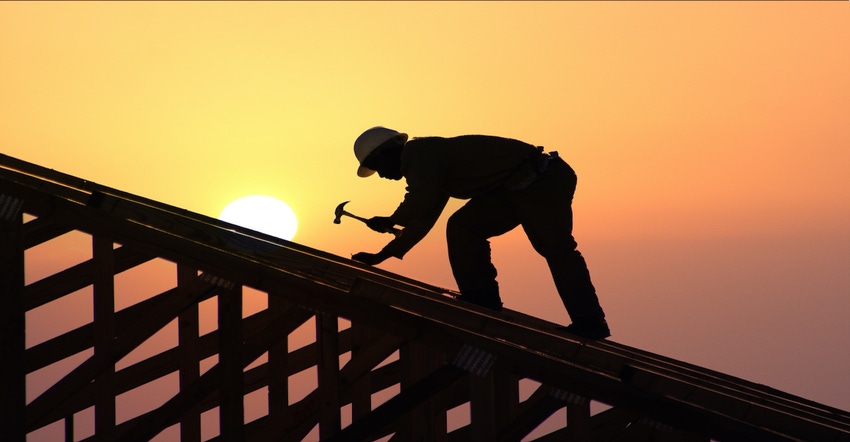 Roofer hammering while the sun sets behind him