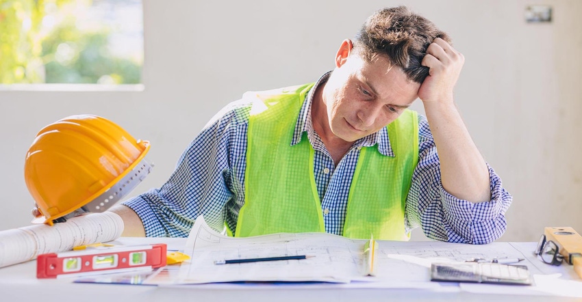 A construction worker stresses out over a set of blueprints