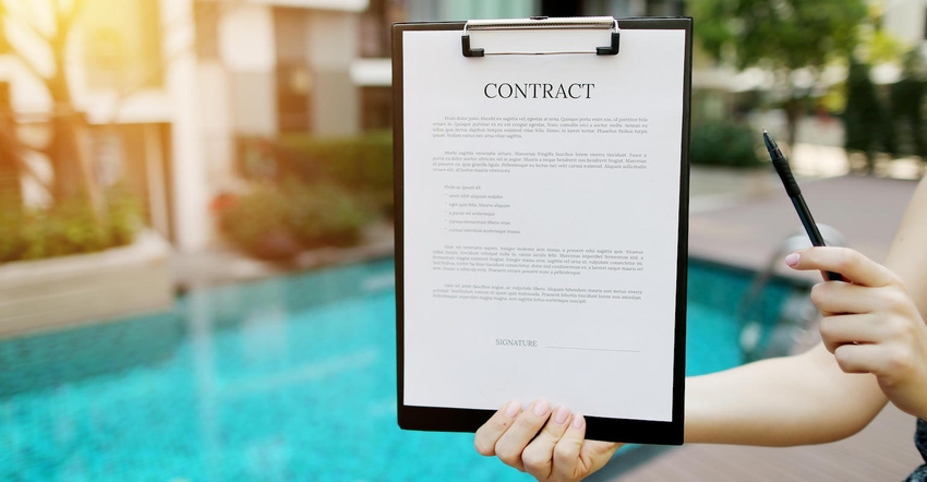 Close-up of woman proposes to sign contract against background of new building with swimming pool. Front used with Open Font
