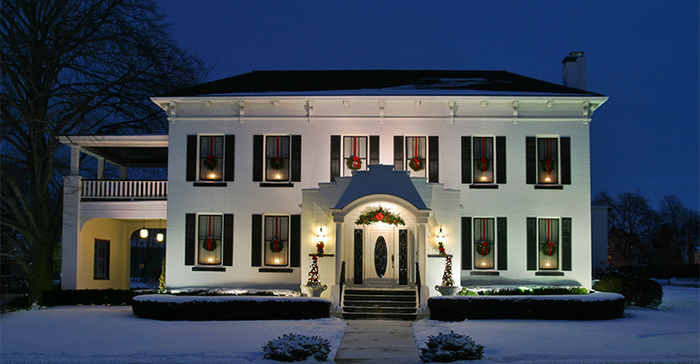 Holiday House. White house at dusk with candles wreaths in the windows.