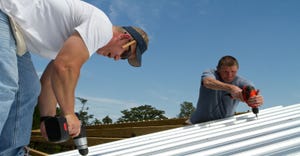 Construction roofing crew uses power tools to screw and fasten sheet metal to the roof rafters of a building.