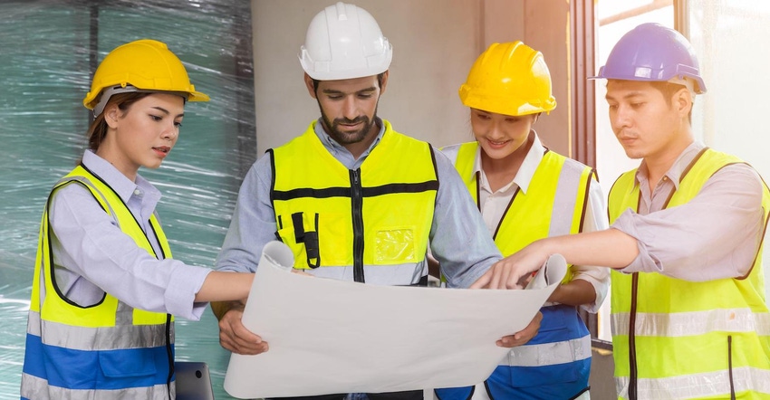Four construction team members review a blueprint together wearing high-visibility yellow vests and hard hats