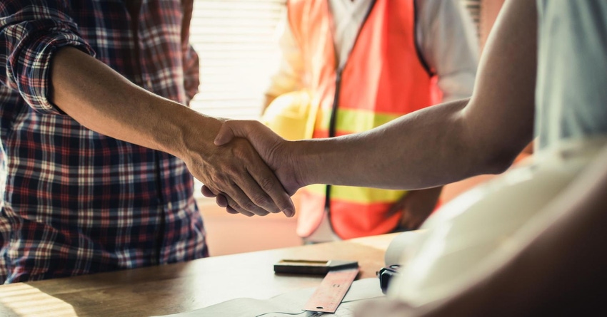 Two construction professionals shake hands over a blueprint for a project