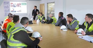 A construction site health and safety briefing takes place in in London site office. Site workers attand with their hard
