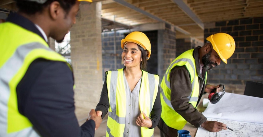 Woman on construction site shakes hands with colleague while another colleague examines architectural plans