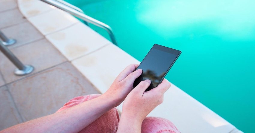 Using mobile phone by the swimming pool, female hands holding smartphone