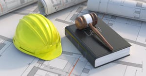 A hard hat and a law book with a gavel on it on top of blueprints