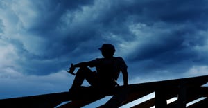 Roofer sitting on a roof during a cloudy day or night