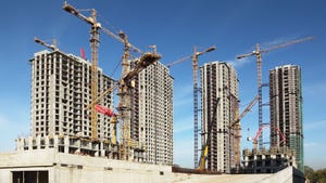 Four tall buildings under construction with cranes against a blue sky