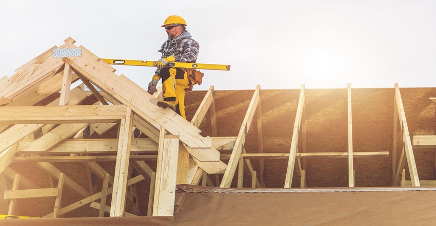 Roofing Contractor with Spirit Level in His Hand on Top of Newly Built Wooden House Roof Structure Roofing Contractor with Spirit Level in His Hand on Top of Newly Built Wooden House Roof Structure