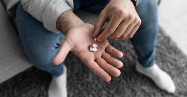 Man holding red and white pills in his open hand