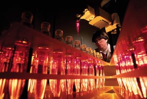 A researcher overlooks a robot arm filling test tubes. 