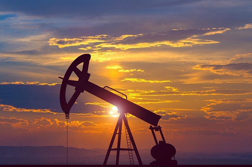 Image show an oil pump on the background of the sunset.