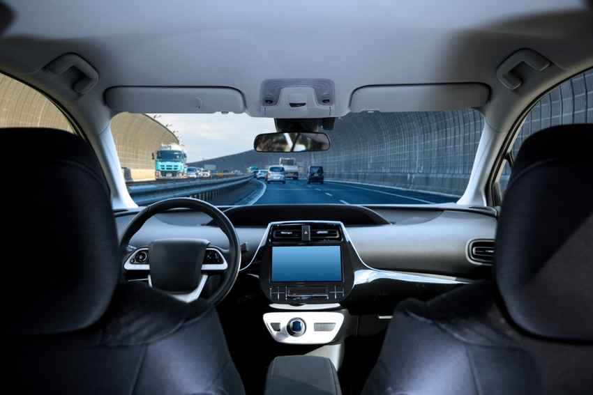 Image shows the cockpit of driverless car driving on highway viewed from rear seat.