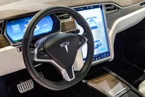 The inside of a Tesla showing the steering wheel and dashboard.