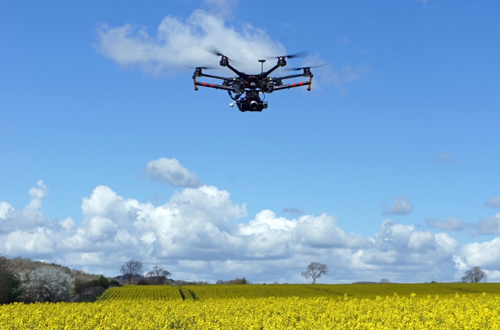 Image shows a drone with camera in a field.