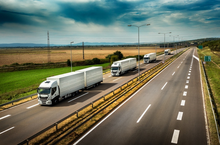 Image shows a caravan or convoy of trucks in line on a country highway.