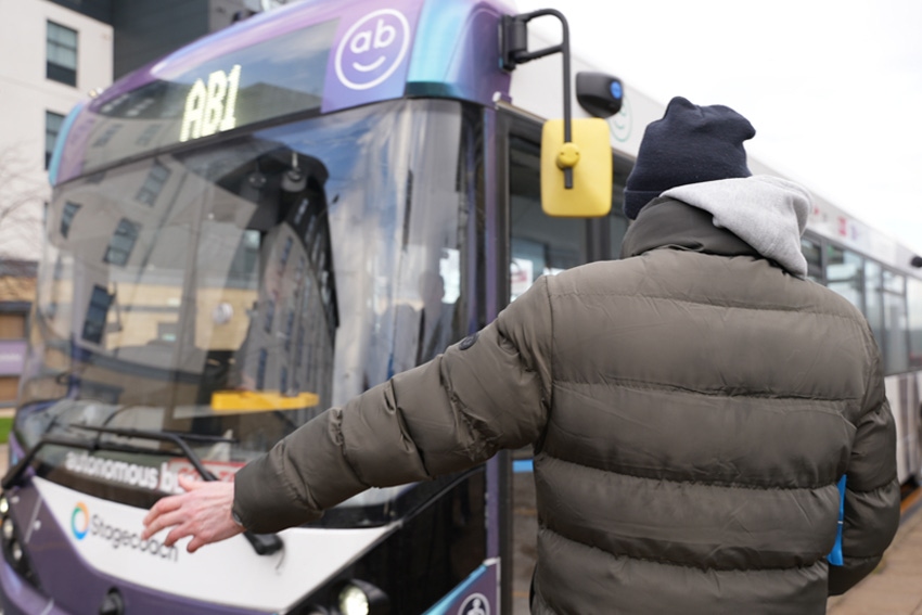 Image shows a man in front of the first self-driving bus to his the road in the U.K.