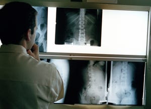 A stock photo of a doctor looking at x-rays on lightboxes.