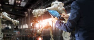 Image shows industrial engineer using tablet to check and control automation robot arms 