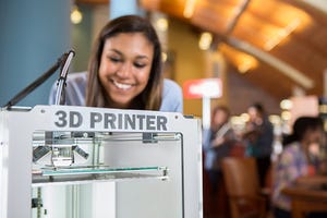 Image shows a 3D printer being used by college student in library makerspace