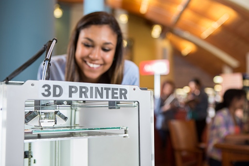 Image shows a 3D printer being used by college student in library makerspace