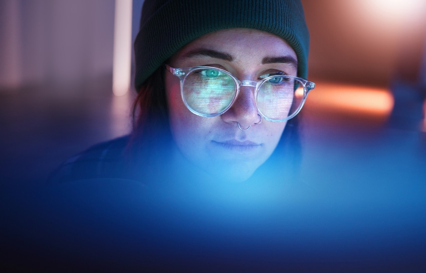 A woman hacker with glasses reflecting a laptop display