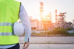 Image shows a man with a safety hat standing near an oil refinery.